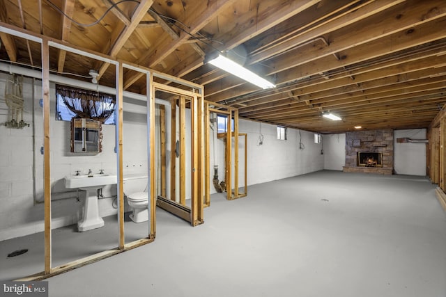 unfinished below grade area with a baseboard heating unit, a stone fireplace, and a sink