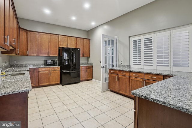 kitchen with light stone counters, brown cabinets, black refrigerator with ice dispenser, a sink, and light tile patterned flooring