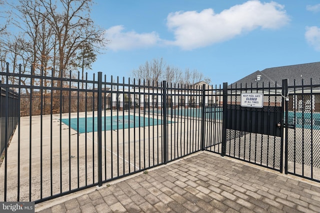 pool with a patio area, fence, and a gate