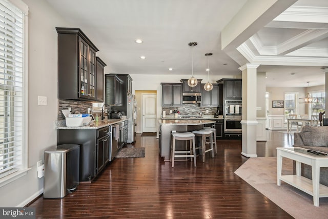 kitchen with a breakfast bar, a kitchen island, a sink, appliances with stainless steel finishes, and ornate columns