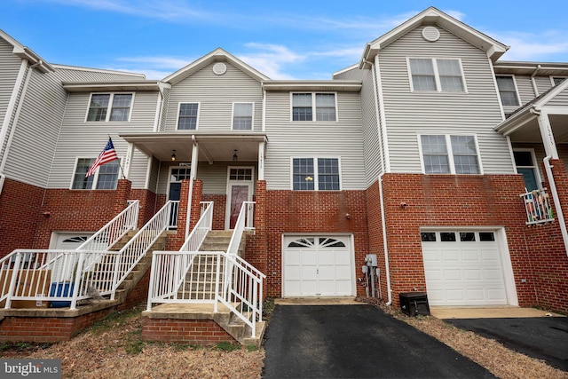 townhome / multi-family property featuring brick siding, aphalt driveway, stairway, a porch, and a garage