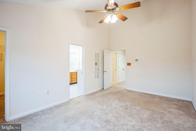 unfurnished bedroom with ensuite bath, a high ceiling, light colored carpet, and baseboards