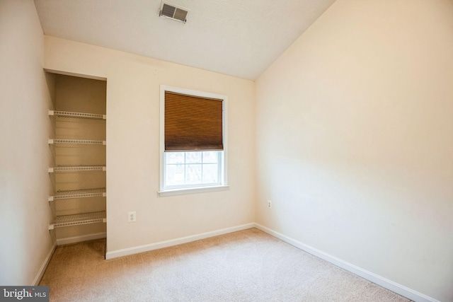 carpeted spare room featuring lofted ceiling, baseboards, and visible vents