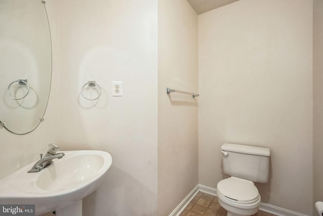 half bath with toilet, baseboards, and a sink