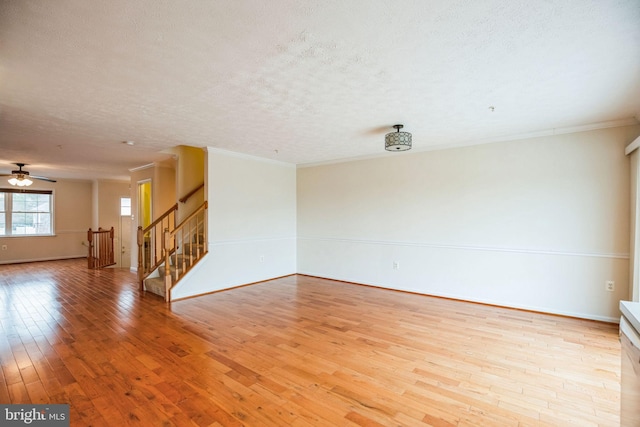 empty room featuring a textured ceiling, light wood-style flooring, stairs, and crown molding