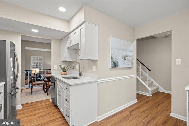 kitchen featuring light wood finished floors, appliances with stainless steel finishes, a sink, and white cabinetry