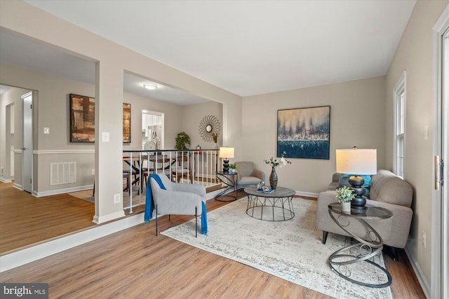 living area with an upstairs landing, wood finished floors, visible vents, and baseboards