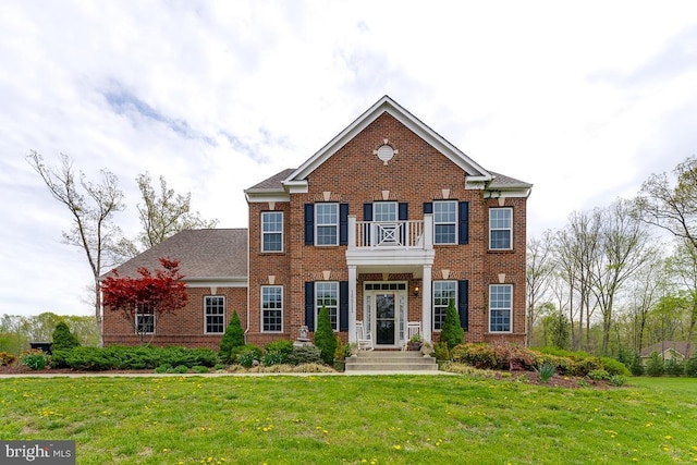 view of front of property featuring brick siding, a front lawn, and a balcony