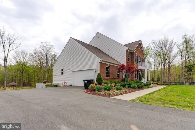 view of side of home featuring brick siding, a lawn, an attached garage, a balcony, and driveway