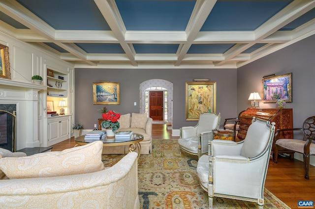 living area featuring a premium fireplace, beam ceiling, arched walkways, and wood finished floors