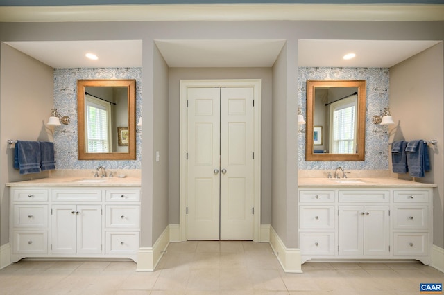 full bath with baseboards, two vanities, and a sink