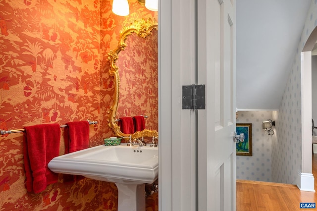 bathroom featuring wallpapered walls, vaulted ceiling, and wood finished floors