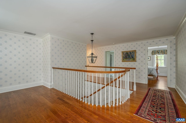 hallway featuring visible vents, ornamental molding, an upstairs landing, wood finished floors, and wallpapered walls