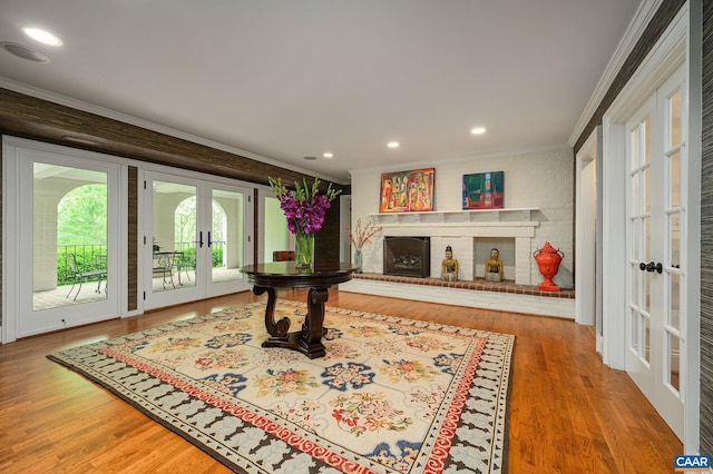 interior space featuring a brick fireplace, wood finished floors, crown molding, and french doors