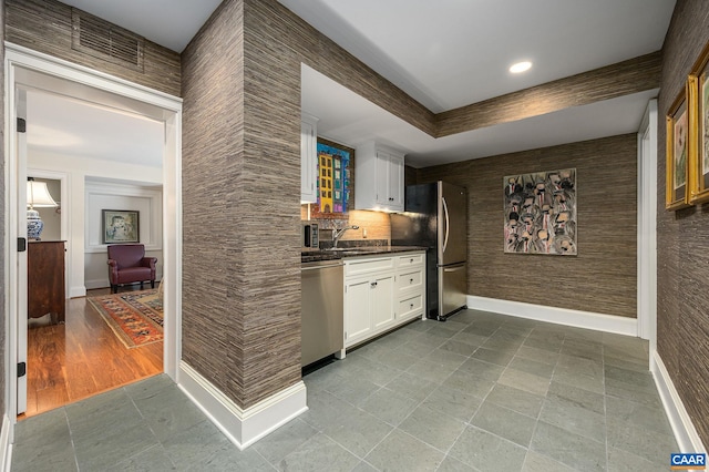 kitchen featuring stainless steel appliances, dark countertops, white cabinetry, a sink, and baseboards