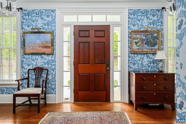 entryway with plenty of natural light, wood finished floors, a notable chandelier, and wallpapered walls