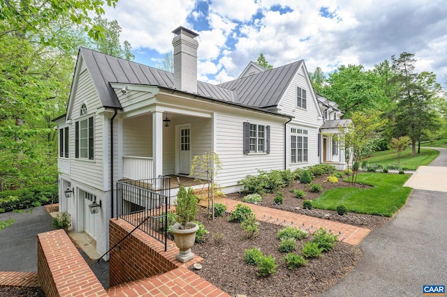 view of front facade with an attached garage, a standing seam roof, a chimney, and metal roof