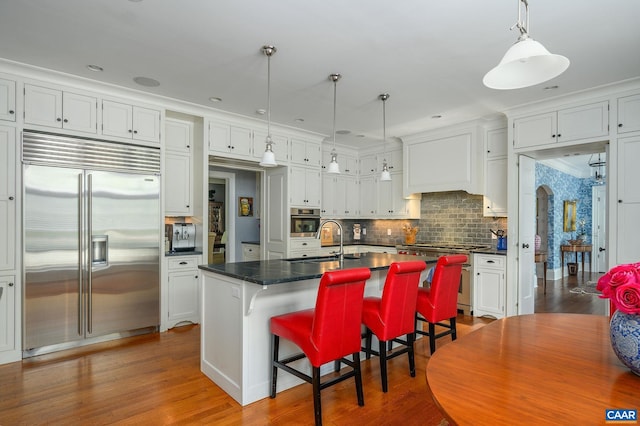 kitchen featuring arched walkways, premium appliances, wood finished floors, a sink, and dark countertops