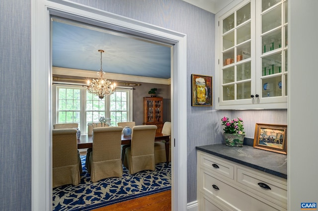 dining area with dark wood-type flooring, a notable chandelier, ornamental molding, and wallpapered walls