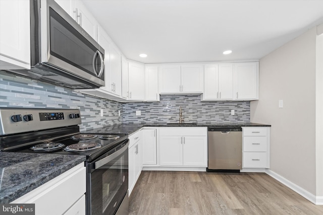 kitchen featuring light wood finished floors, a sink, stainless steel appliances, white cabinets, and backsplash