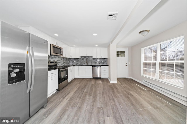 kitchen with dark countertops, tasteful backsplash, light wood-type flooring, white cabinets, and stainless steel appliances