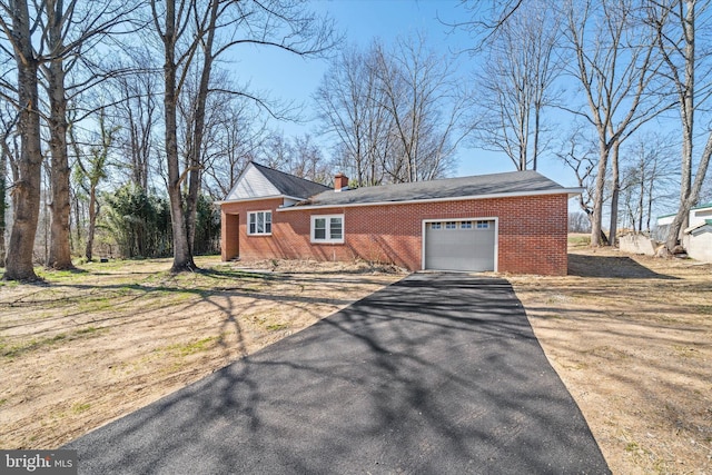 view of front of home featuring brick siding, an attached garage, a chimney, and aphalt driveway