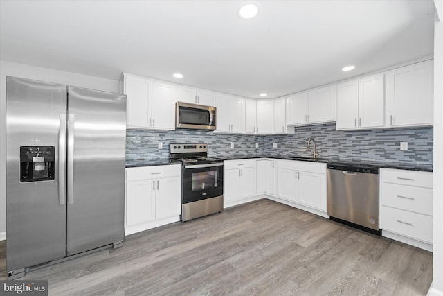 kitchen with light wood-type flooring, tasteful backsplash, dark countertops, and appliances with stainless steel finishes