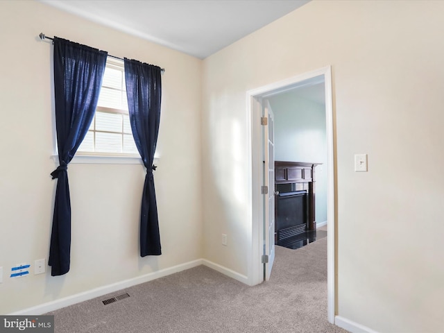 empty room with carpet, a fireplace with flush hearth, visible vents, and baseboards