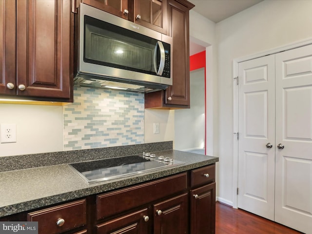 kitchen featuring black electric stovetop, dark brown cabinetry, decorative backsplash, stainless steel microwave, and dark countertops