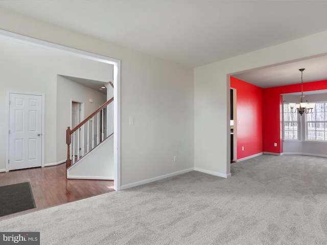 carpeted empty room featuring a chandelier, stairway, and baseboards