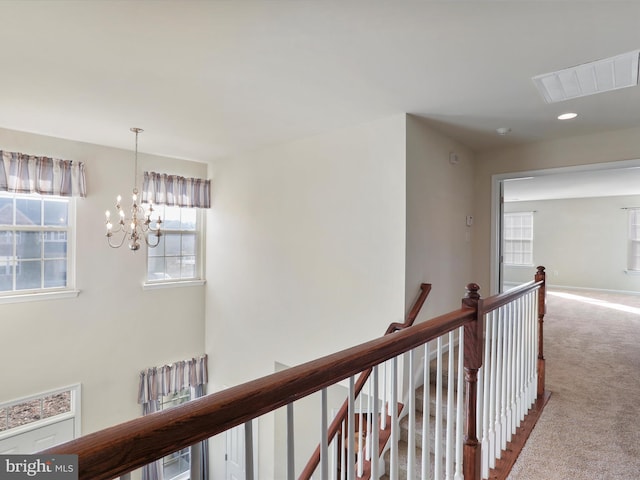 corridor featuring carpet floors, visible vents, baseboards, an upstairs landing, and an inviting chandelier