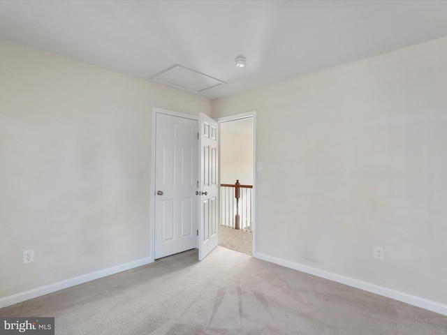 carpeted spare room featuring attic access and baseboards