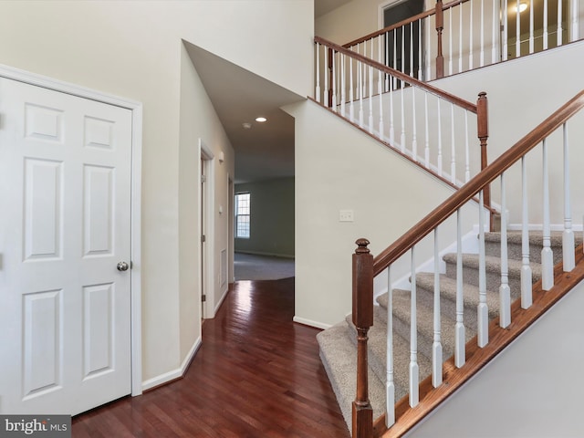 staircase with a high ceiling, baseboards, and wood finished floors