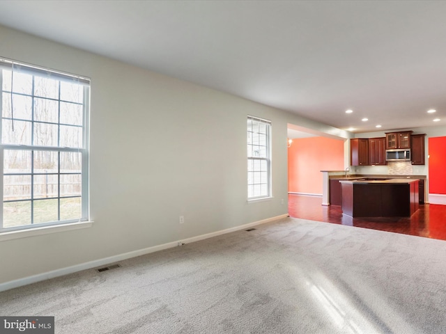 kitchen featuring visible vents, baseboards, stainless steel microwave, open floor plan, and dark colored carpet