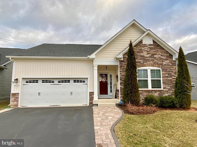 craftsman-style home with roof with shingles, a garage, stone siding, driveway, and a front lawn