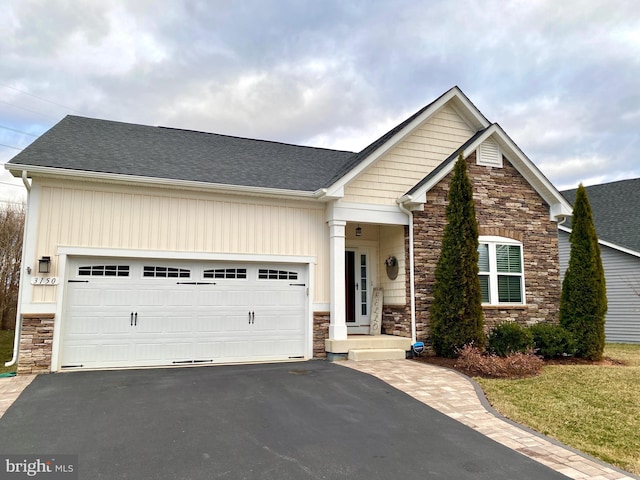 craftsman-style house with a garage, stone siding, aphalt driveway, and roof with shingles