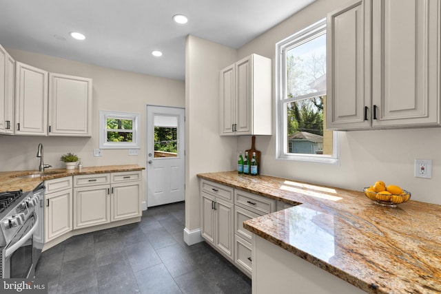 kitchen with light stone counters, gas stove, a sink, white cabinetry, and recessed lighting