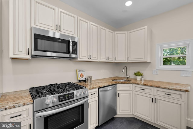 kitchen featuring white cabinets, stainless steel appliances, light stone countertops, and a sink