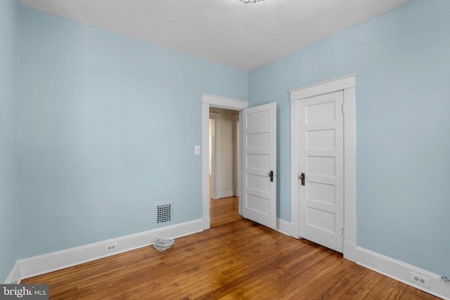 unfurnished bedroom with baseboards, wood finished floors, and visible vents
