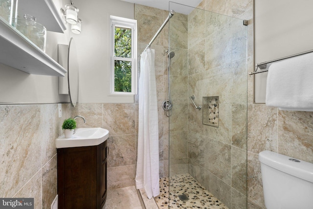 bathroom featuring wainscoting, a tile shower, vanity, toilet, and tile walls