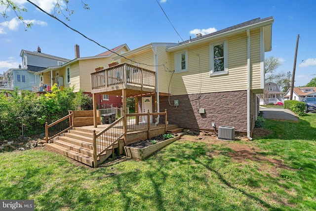 rear view of property featuring central AC, stone siding, a wooden deck, a balcony, and a lawn