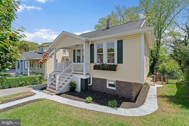 bungalow with fence, roof with shingles, a front yard, a chimney, and covered porch