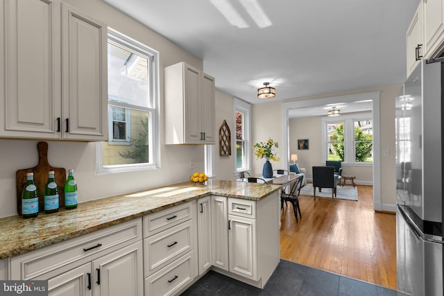 kitchen featuring white cabinets, light stone countertops, freestanding refrigerator, a peninsula, and dark wood-style floors