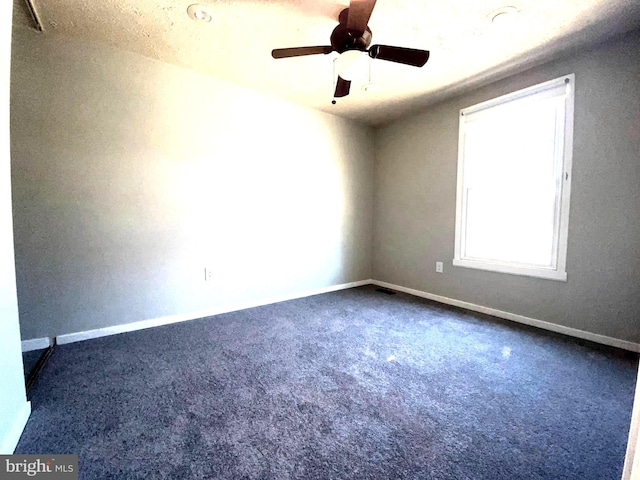 spare room with dark colored carpet, ceiling fan, and baseboards