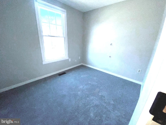 spare room with baseboards, visible vents, and dark carpet