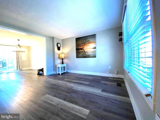 spare room with a notable chandelier, a textured ceiling, baseboards, and wood finished floors