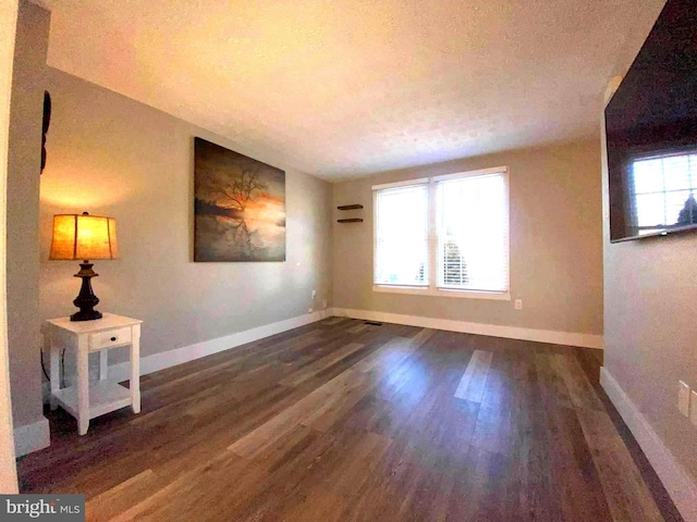 empty room with a textured ceiling, wood finished floors, and baseboards