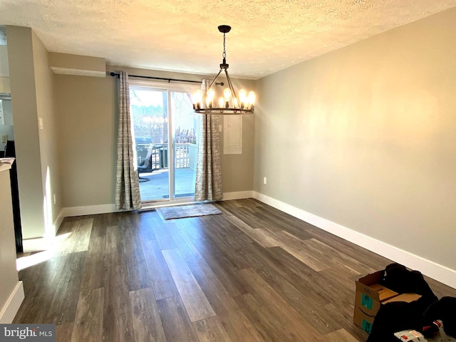 unfurnished dining area with dark wood-style floors, a chandelier, a textured ceiling, and baseboards