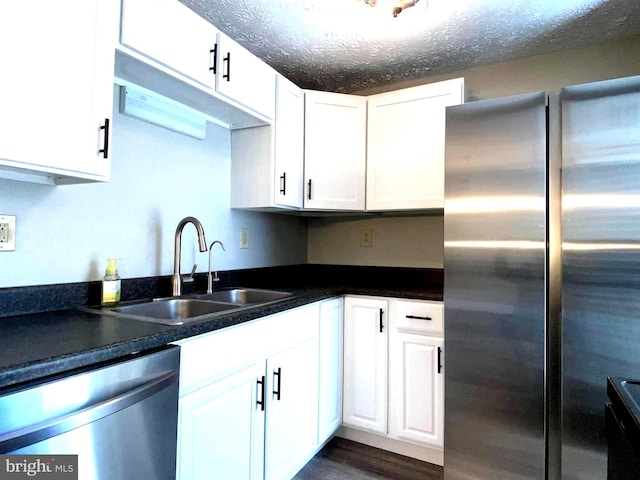 kitchen with dark wood finished floors, appliances with stainless steel finishes, white cabinets, a sink, and a textured ceiling