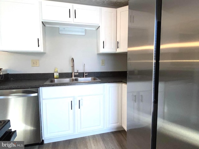 kitchen featuring white cabinets, dark countertops, stainless steel appliances, and a sink